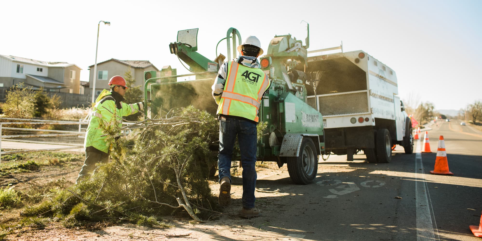 Workers feeding branches into a roadside wood chipper beside a truck.
