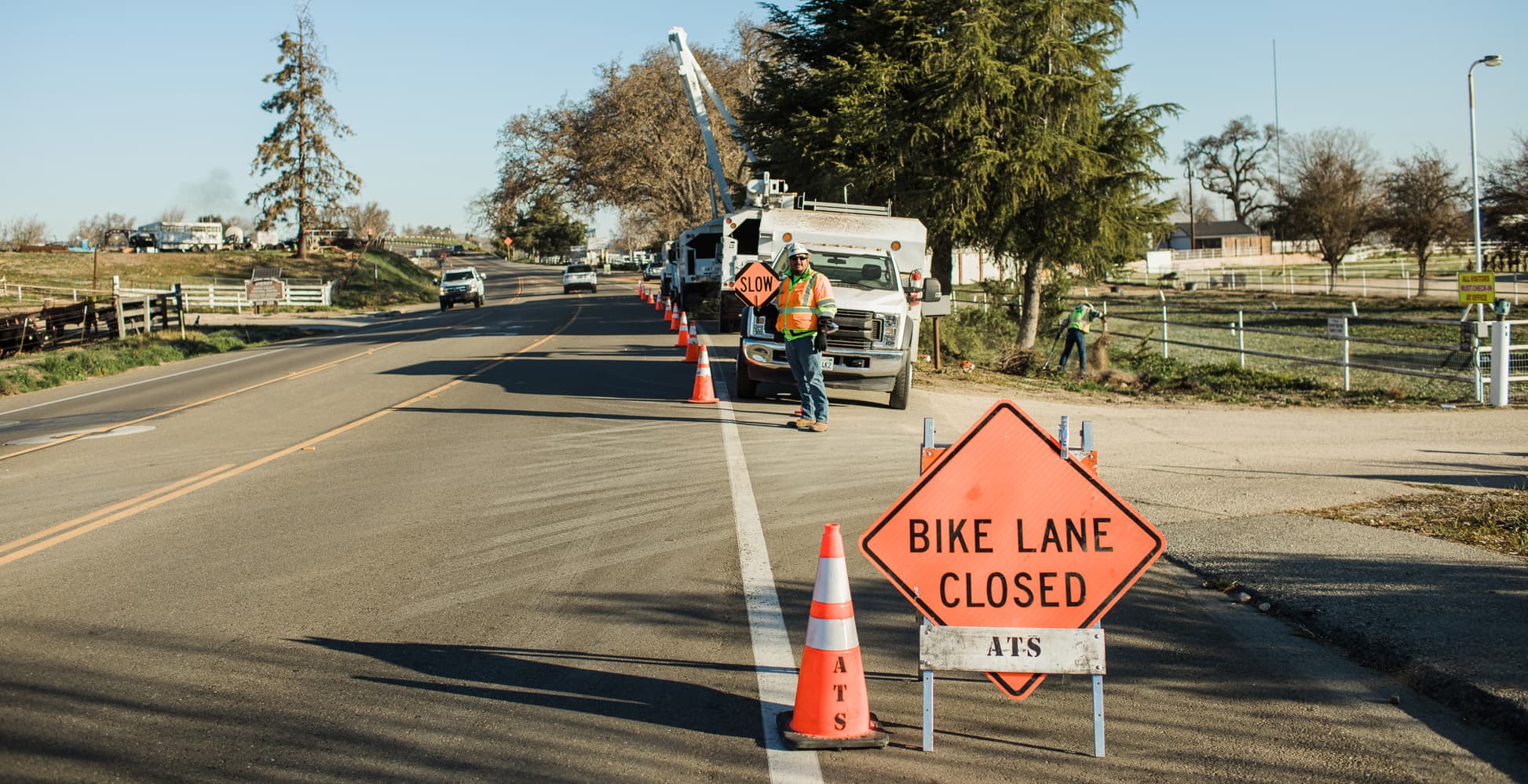 Bike Lane Closed sign and traffic cones beside tree-service trucks.