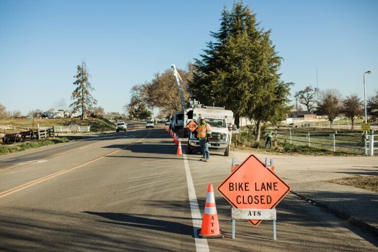 Bike Lane Closed sign and traffic cones beside tree-service trucks.