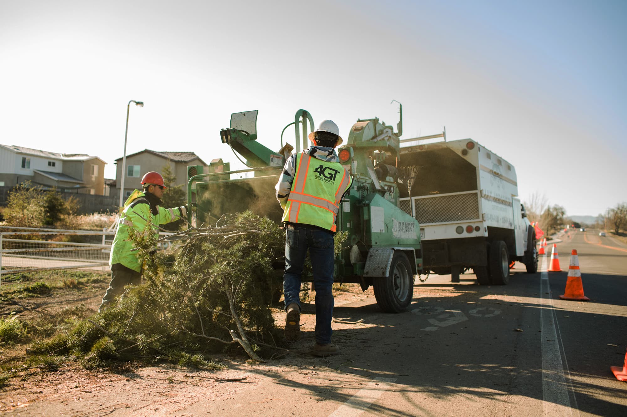 Workers feeding branches into a roadside wood chipper beside a truck.